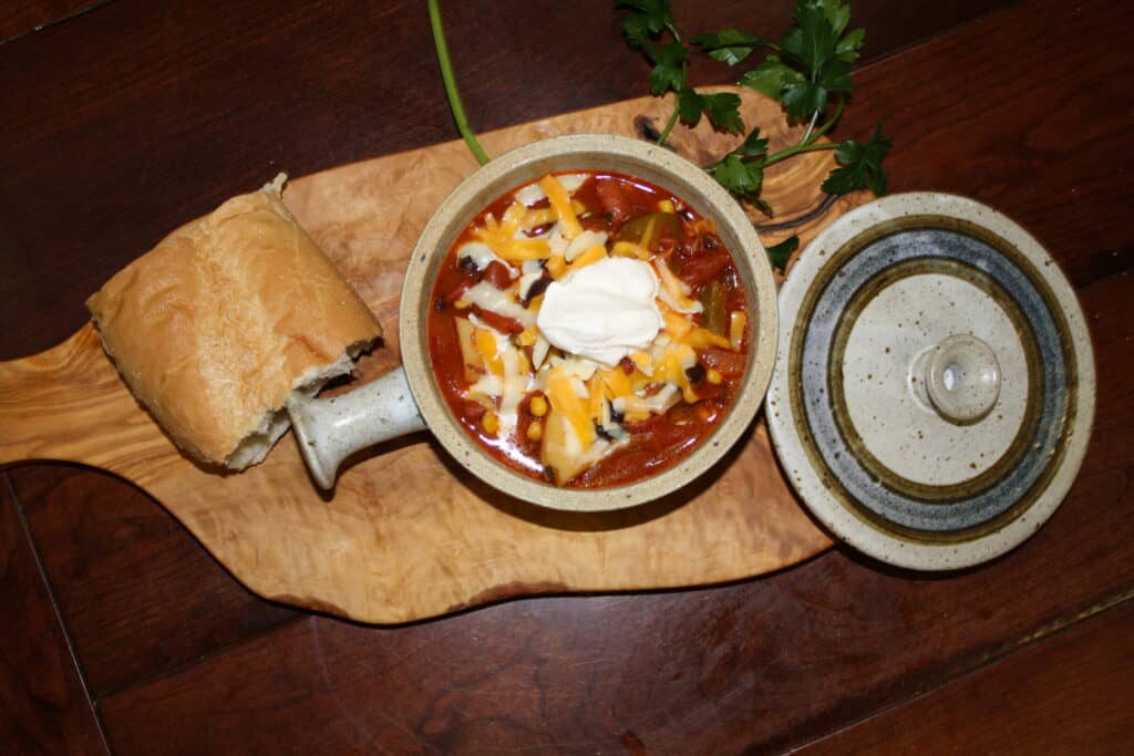 Veggie Chili in a crock with french bread and fresh parsley near by.