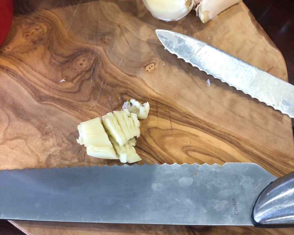 Mincing garlic on a cutting board with a knife