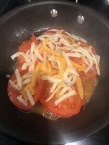 Adding cheese to sliced tomatoes sautéing in a skillet.