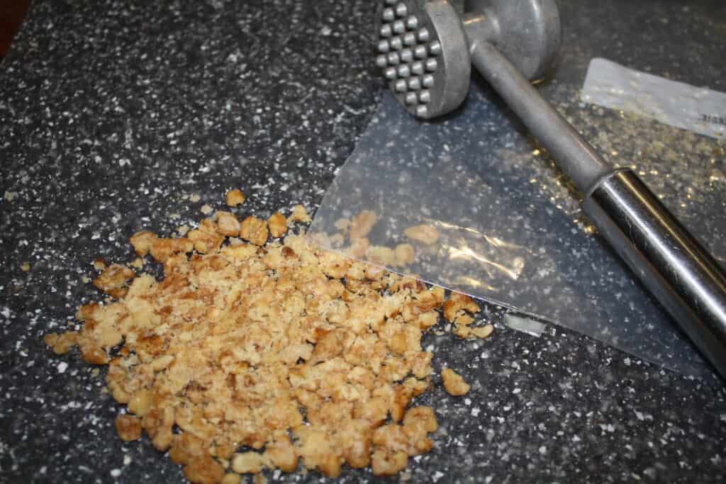 Crushed walnuts & a meat tenderizer on a cutting board
