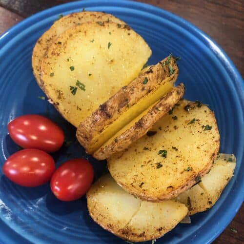 Hasselback Potateo on a blue plate with cherry tomatoes