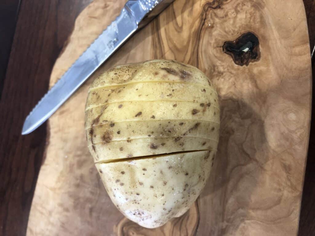 Slicing a hasselback potato vertically on wood cutting board with a knife.