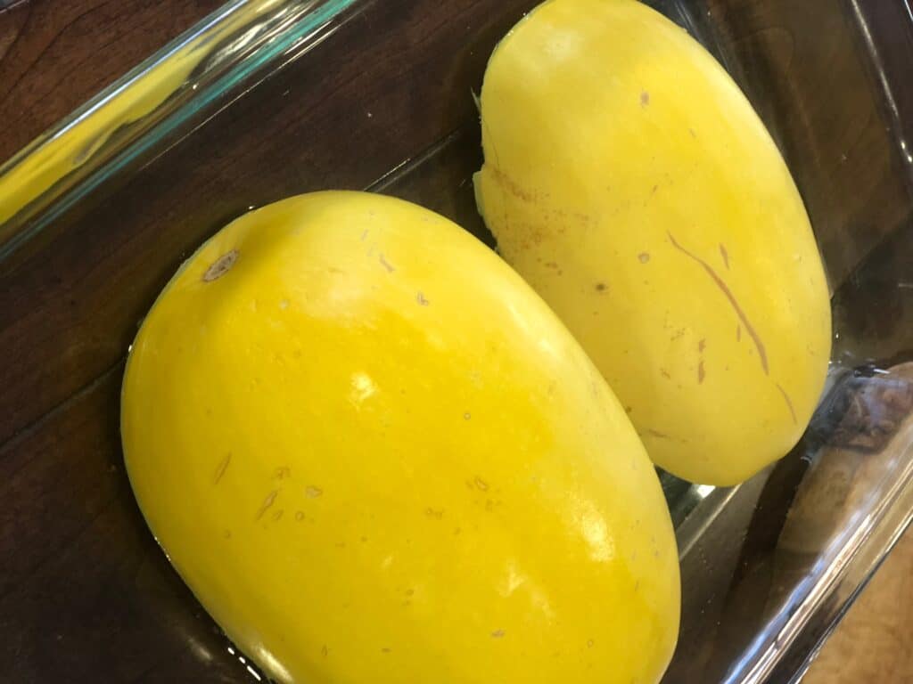 Spaghetti Squash sliced in half, face down in a baking pan.