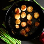 Pan-Fried Scallops in a cast-iron pan with asparagus off to the side