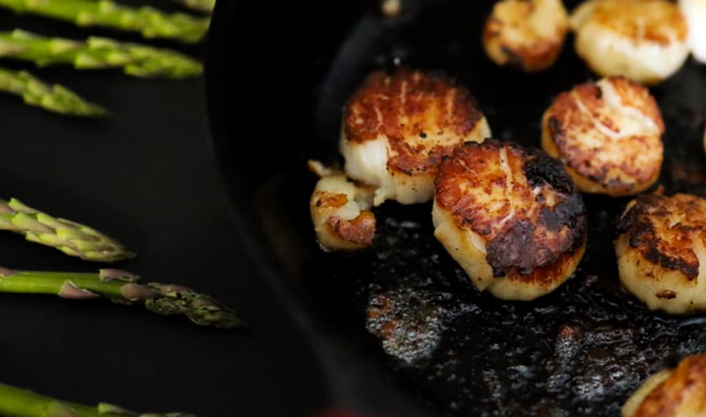 Pan-Fried Scallops in a cast-iron pan with asparagus off to the side