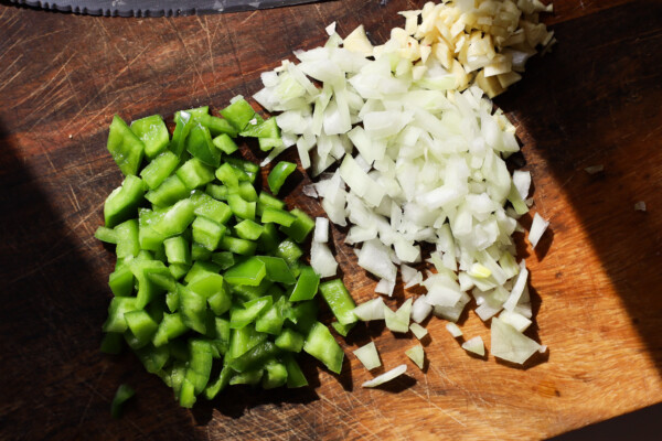 Diced green pepper, onion and garlic on a cutting board .