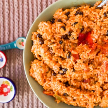 Easy Cheesy Spanish Rice with Black beans in a green bowl with colorful measuring spoons to the side.