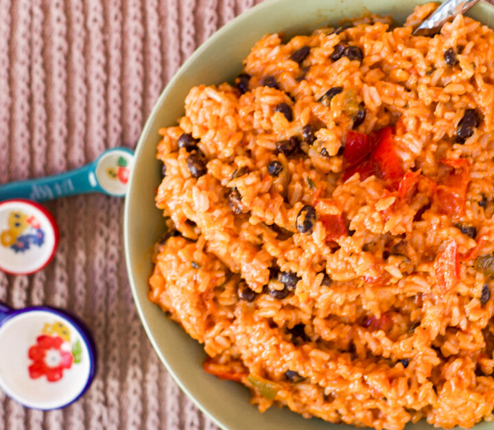 Easy Cheesy Spanish Rice with Black beans in a green bowl with colorful measuring spoons to the side.