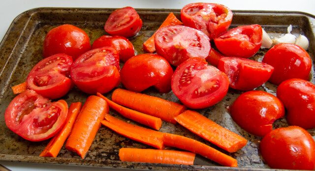 Tomatos and carrots cut for roasting in the oven on a backing sheet.