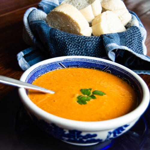 Roasted tomato feta soup in a blue and white bowl with french bread off to the side.