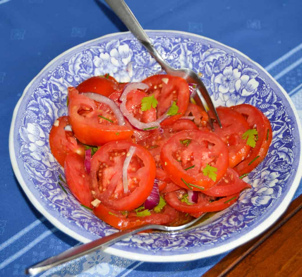 Summer tomato Salad in a blue and white bowl with serving utensils 