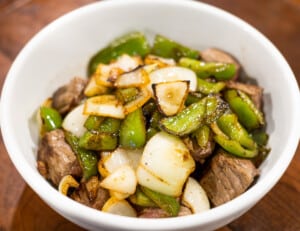 Sautéed onions and peppers over grilled beef in a bowl.